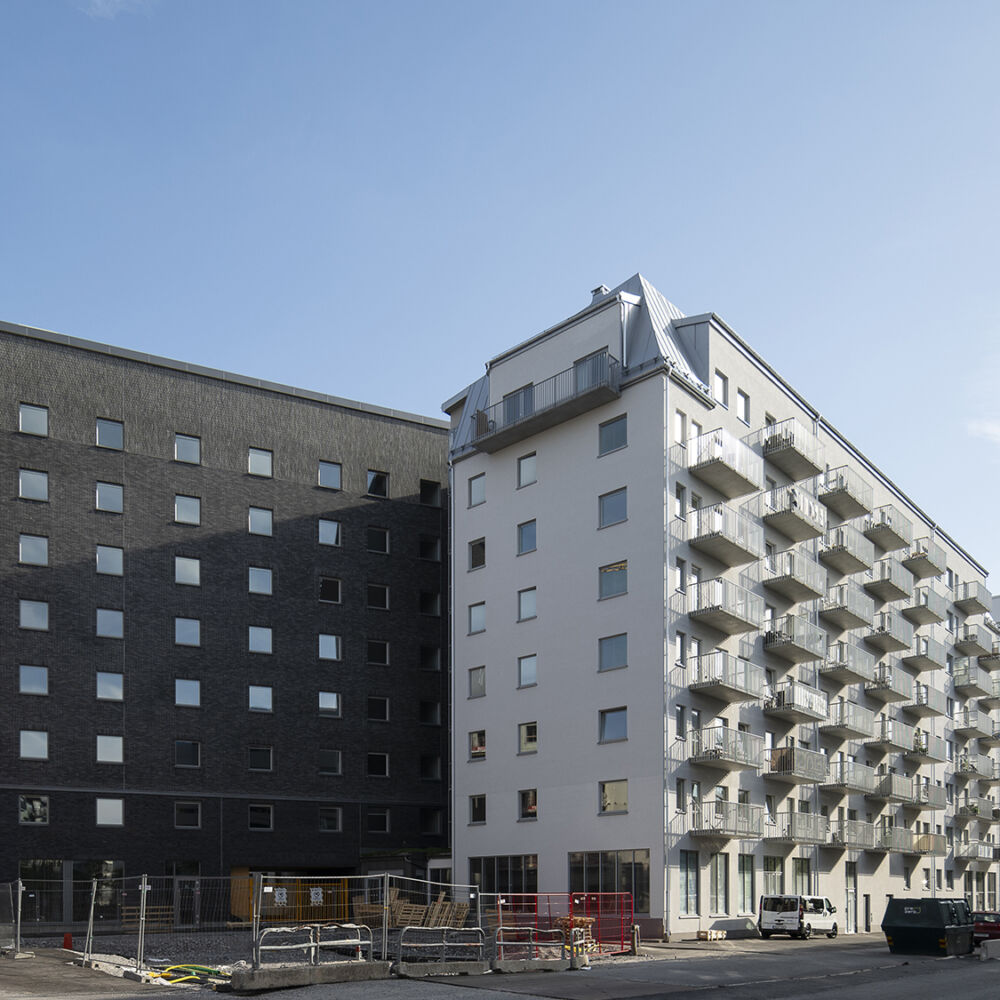 Nybyggda flervåningshus, ett i mörkt tegel och ett med vit puts och balkonger.