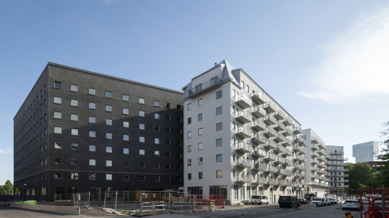 Nybyggda flervåningshus, ett i mörkt tegel och ett med vit puts och balkonger.