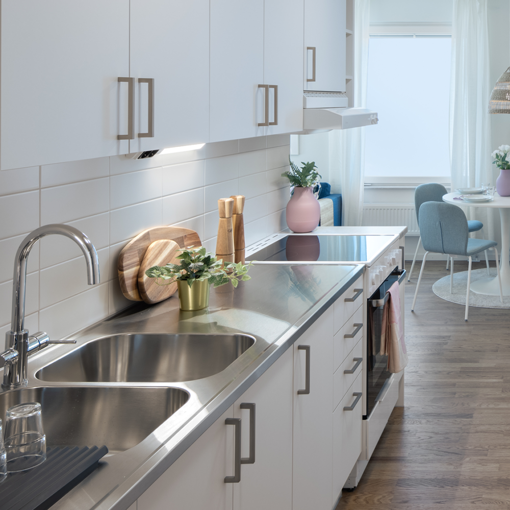 Modern kök med vita skåp, rostfri diskbänk, ekparkett och en matplats med runt bord och gröna stolar