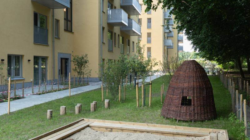 Lekplats, gräsmatta och annan grönska på gården till ett flerbostadshus.